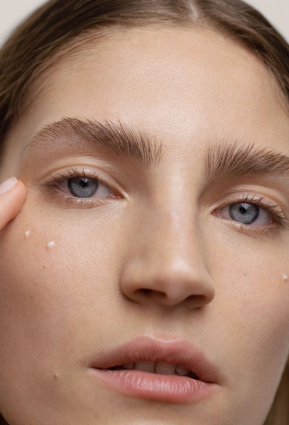 Woman applies eye cream under her eye with ring finger