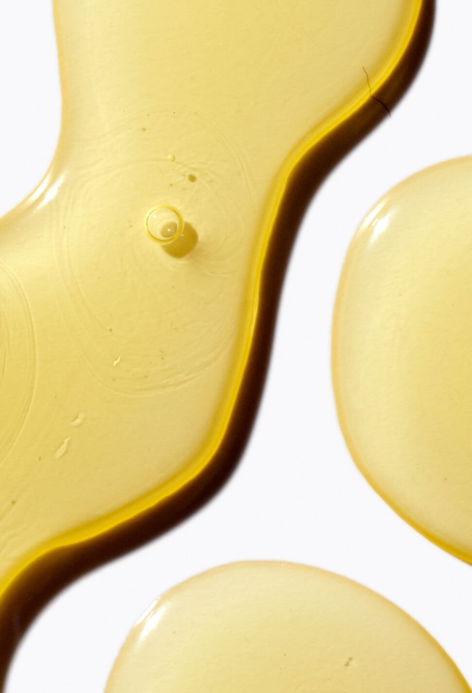 close up of three groups of yellow liquid on white background